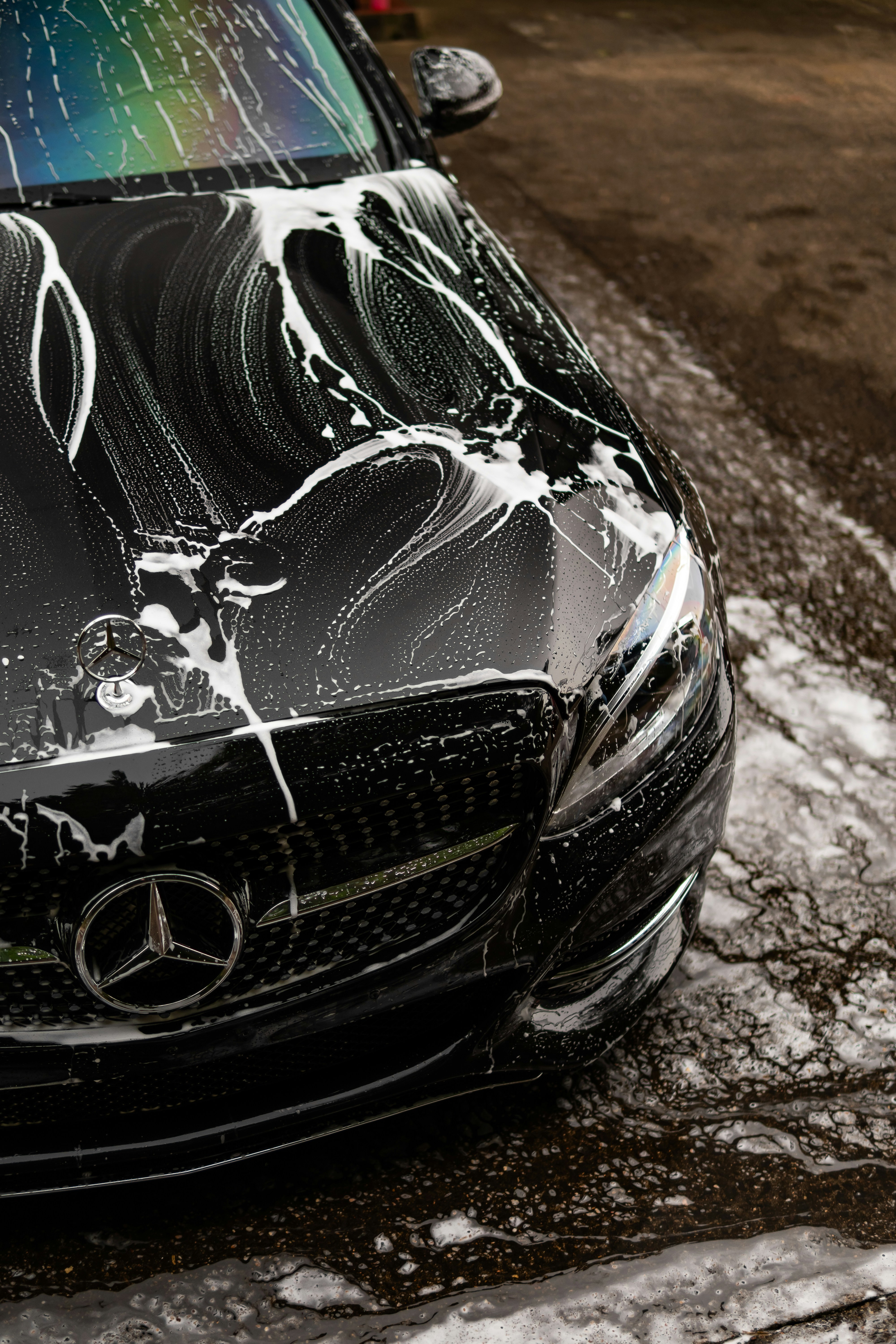 Black Mercedes-Benz covered in soap suds during a professional exterior wash and detail process